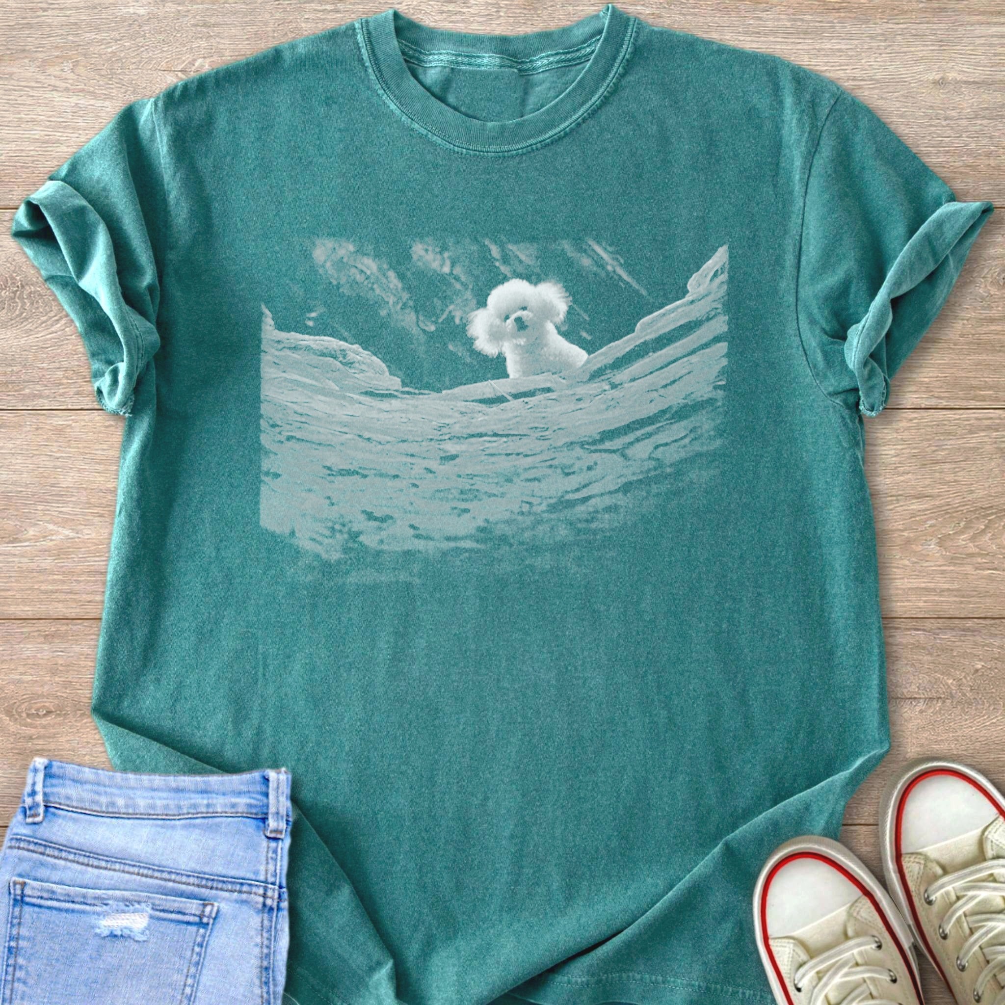 Blue Spruce Comfort Colors 1717 t-shirt with a white graphic of a white fluffy dog from silence of the lambs, peeking over jagged rocks.