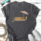 Graphic t-shirt with a dachshund on a beach under an umbrella.