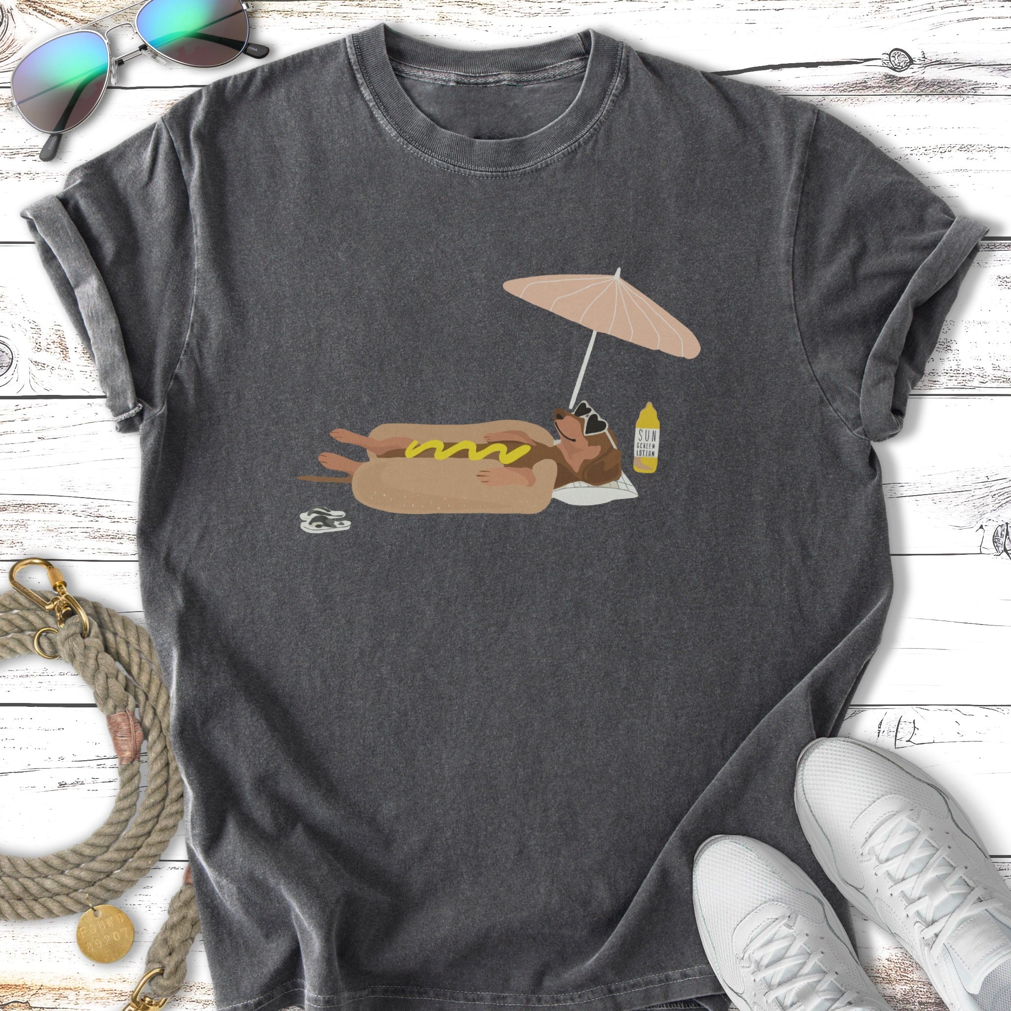 Graphic t-shirt with a dachshund on a beach under an umbrella.