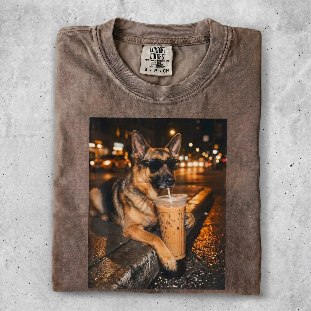 German Shepherd wearing sunglasses drinks iced coffee in a city at night.