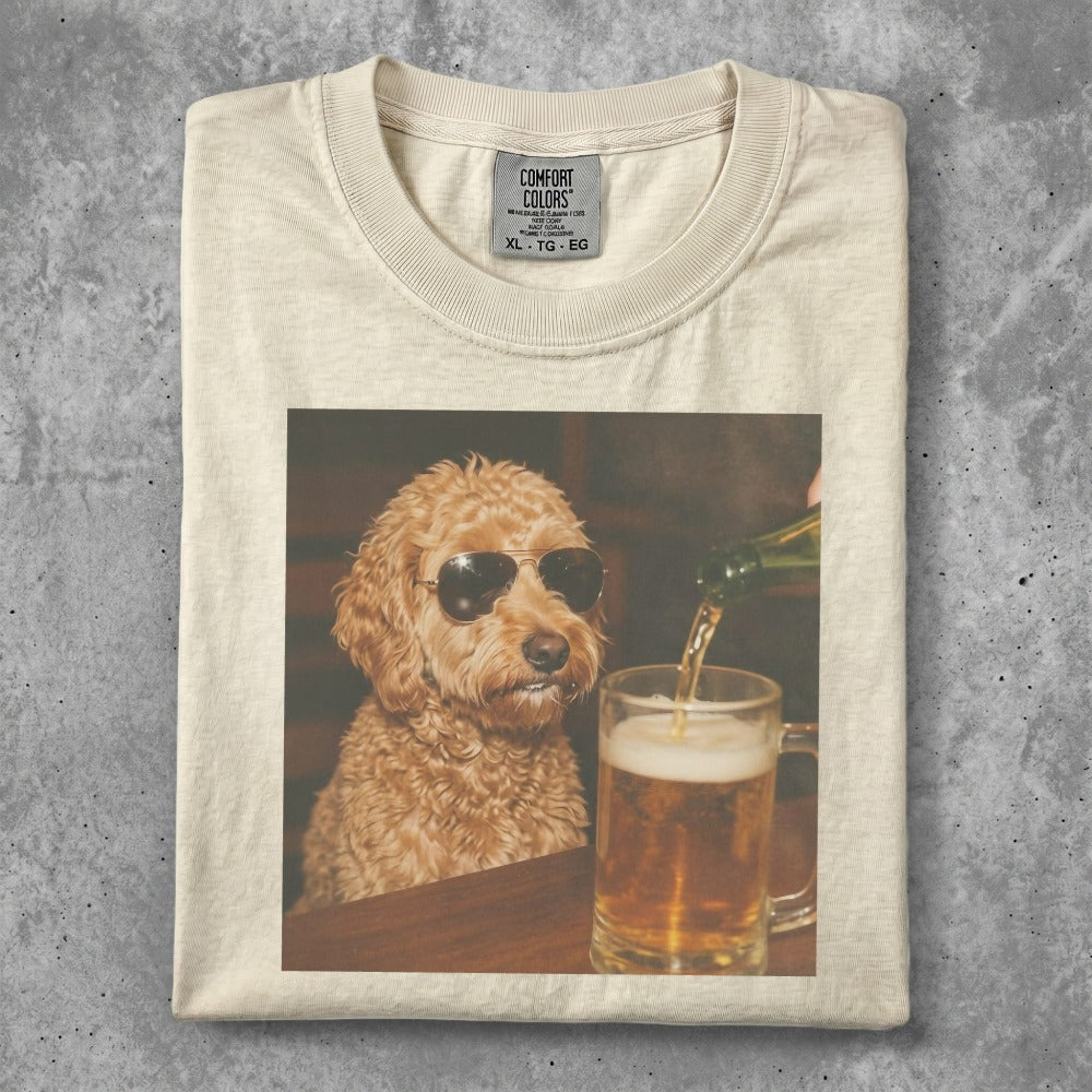 Goldendoodle wearing sunglasses sits at a table with a beer.
