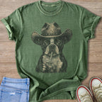 Boston terrier with cowboy hat drinks from a cup on a green t-shirt.