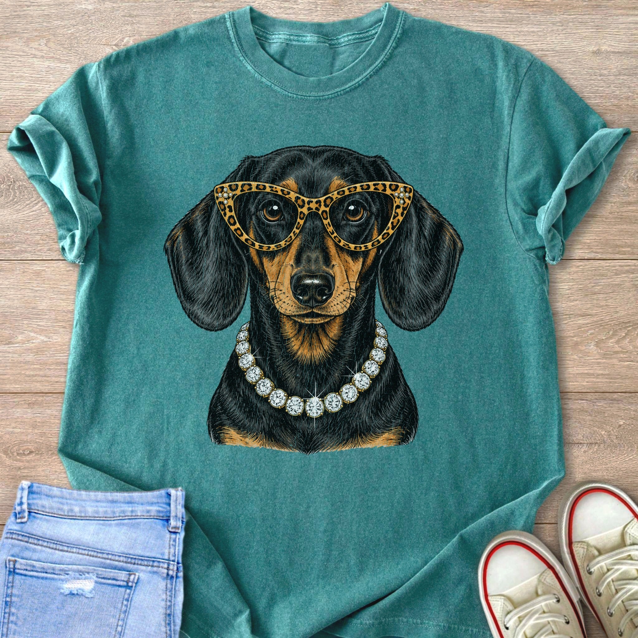 Dachshund wearing leopard print glasses and diamond necklace on teal t-shirt.