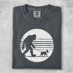 Dark gray t-shirt with Bigfoot walking a dog silhouette on striped circle.