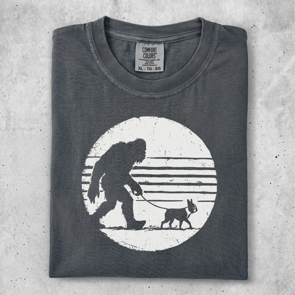 Dark gray t-shirt with Bigfoot walking a dog silhouette on striped circle.