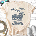 Cream t-shirt with "Real Men Play With Their Weiners" and dachshund graphic.
