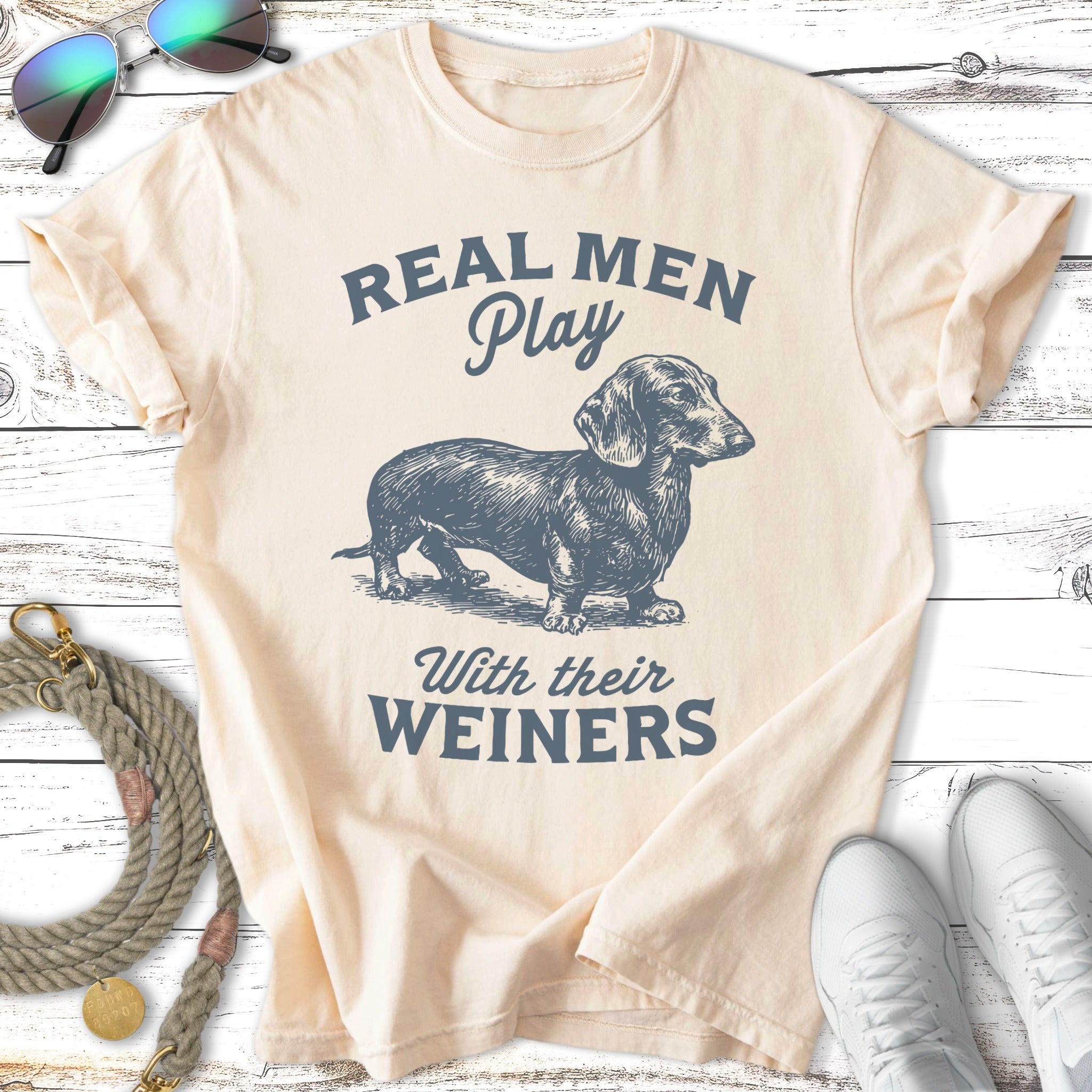 Cream t-shirt with "Real Men Play With Their Weiners" and dachshund graphic.