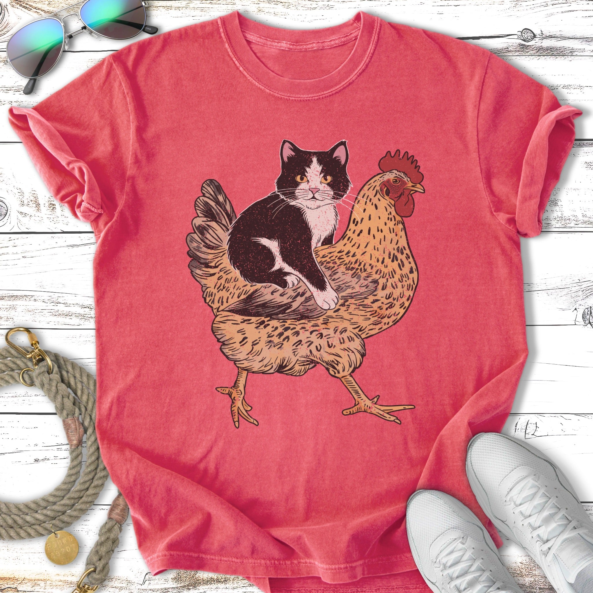 Tuxedo cat riding a chicken, with sunglasses and shoes nearby.