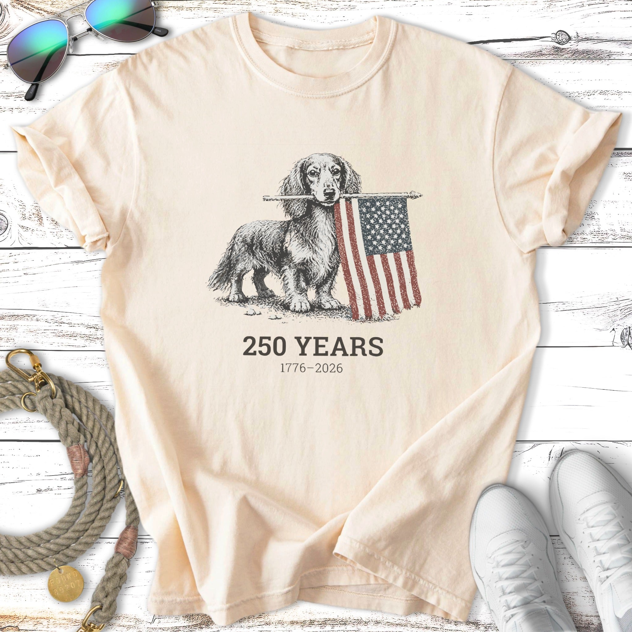 Cream t-shirt with a dachshund holding an American flag, reads "250 Years 1776-2026".