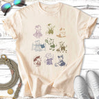 Line art of nine cats in various poses and outfits on a light cream t-shirt.