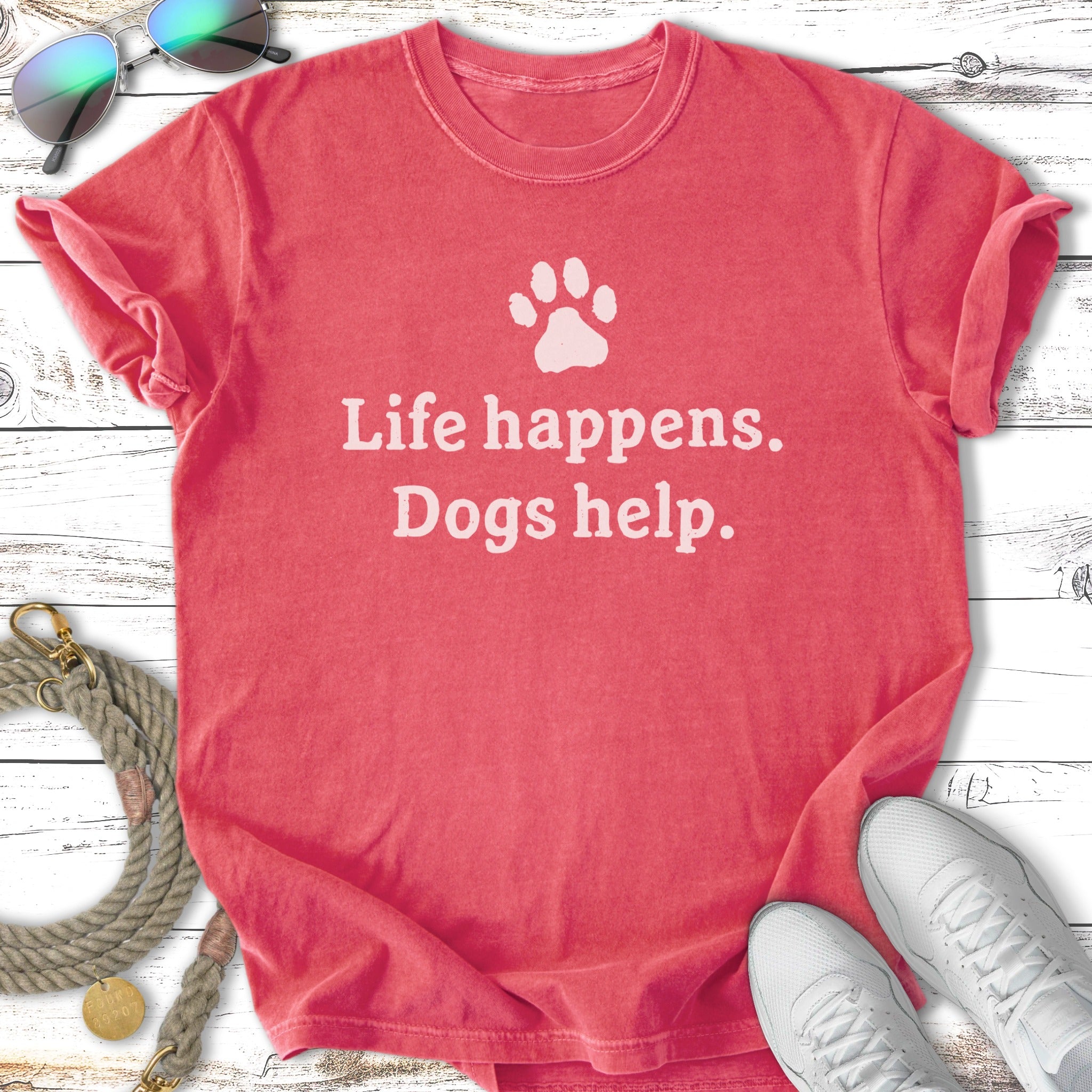Coral t-shirt with white text: "Life happens. Dogs help." and a paw print.