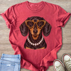 Dachshund wearing leopard glasses and a diamond necklace on a pink t-shirt.