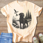 Black Labrador fishing with ducks flying in a forest lake scene on a peach t-shirt.