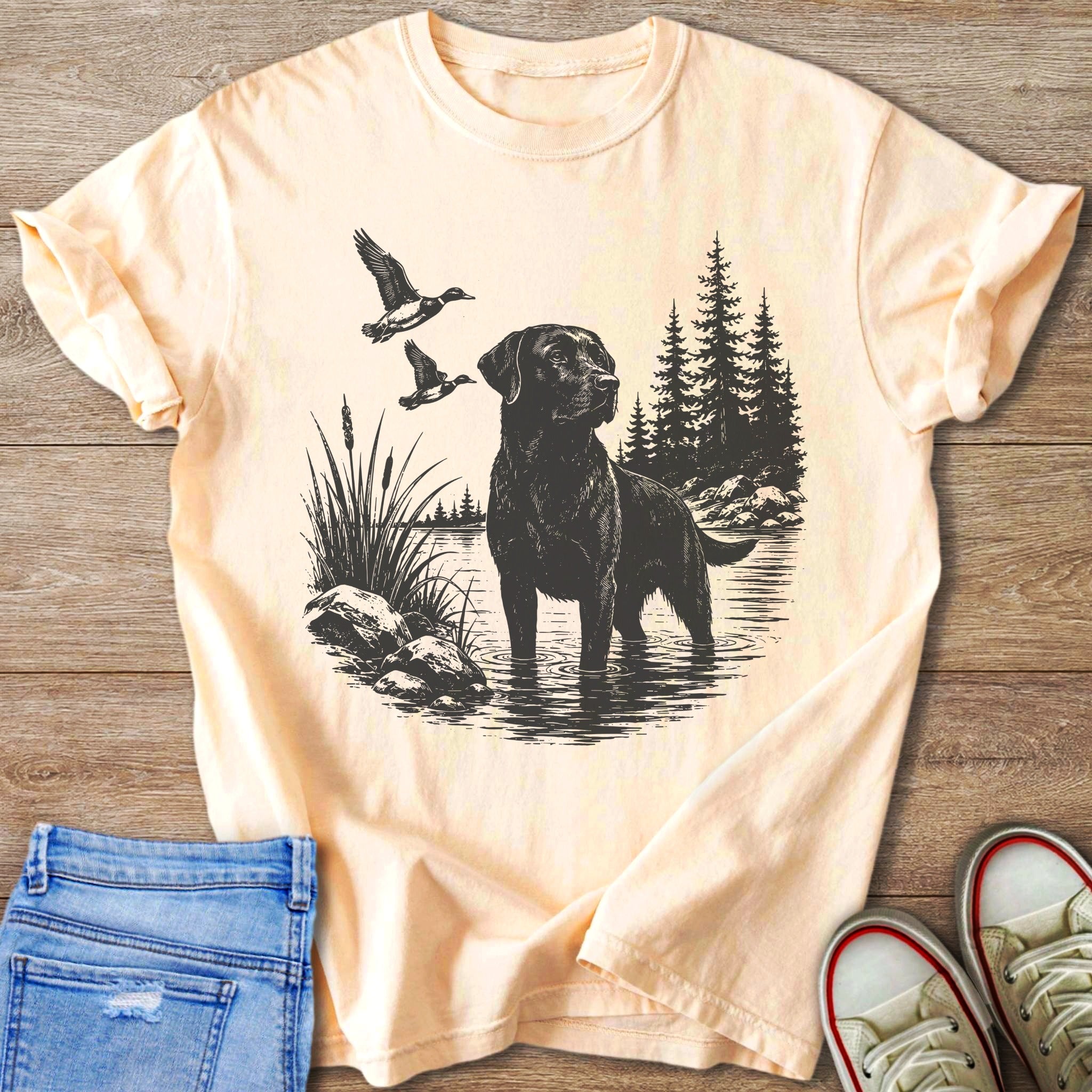 Black Labrador fishing with ducks flying in a forest lake scene on a peach t-shirt.