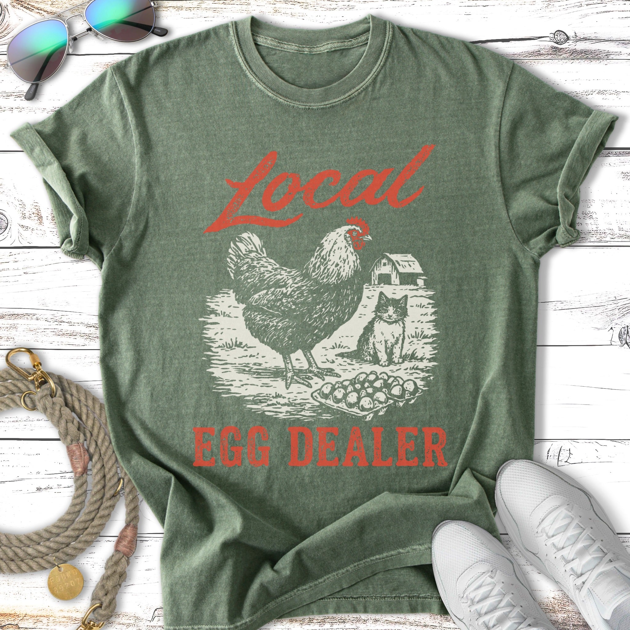 Green t-shirt with "Local Egg Dealer" text and chicken and cat illustration.