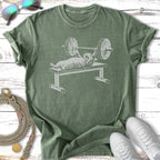 Cat lifting weights on a bench press, printed on a green t-shirt.