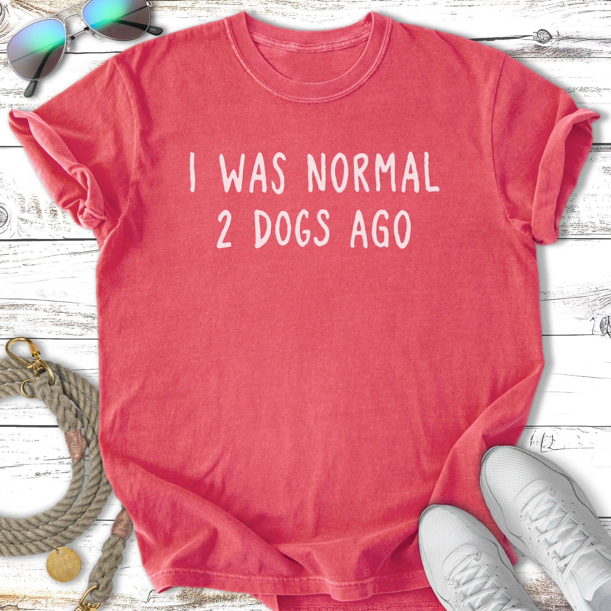 Coral t-shirt with white text "I WAS NORMAL 2 DOGS AGO" and accessories.