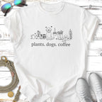 White t-shirt with black line drawing of plants, dogs, coffee cup, and text "plants. dogs. coffee."