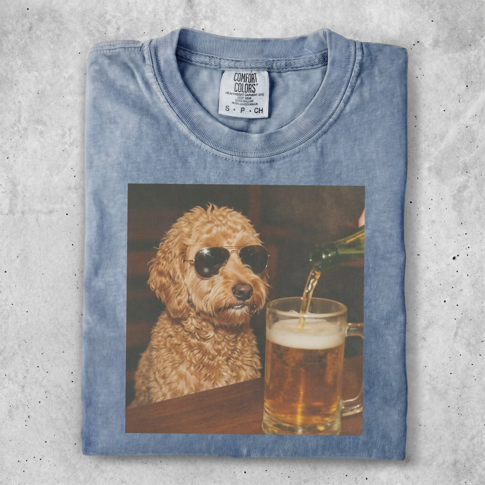 Brown poodle wearing sunglasses sits by a beer mug.