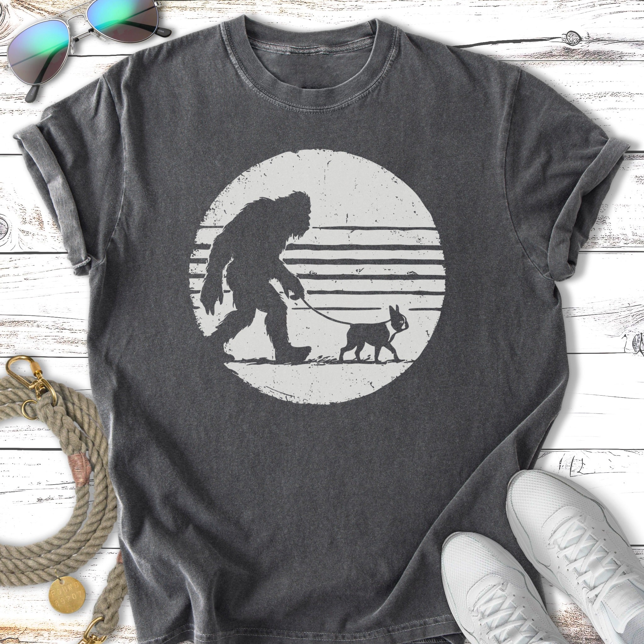 Bigfoot silhouette walks small dog on leash against striped circle background.