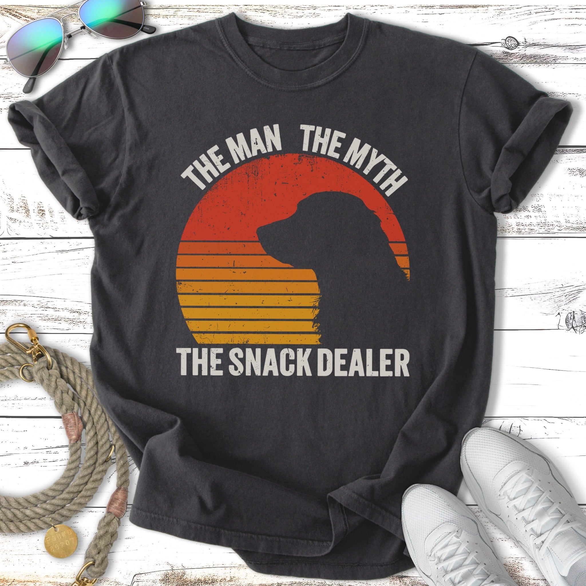 Black t-shirt with sunset graphic, dog silhouette, and text "The Man The Myth The Snack Dealer".