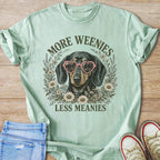 Dachshund in heart glasses surrounded by flowers with text "More Weenies Less Meanies."