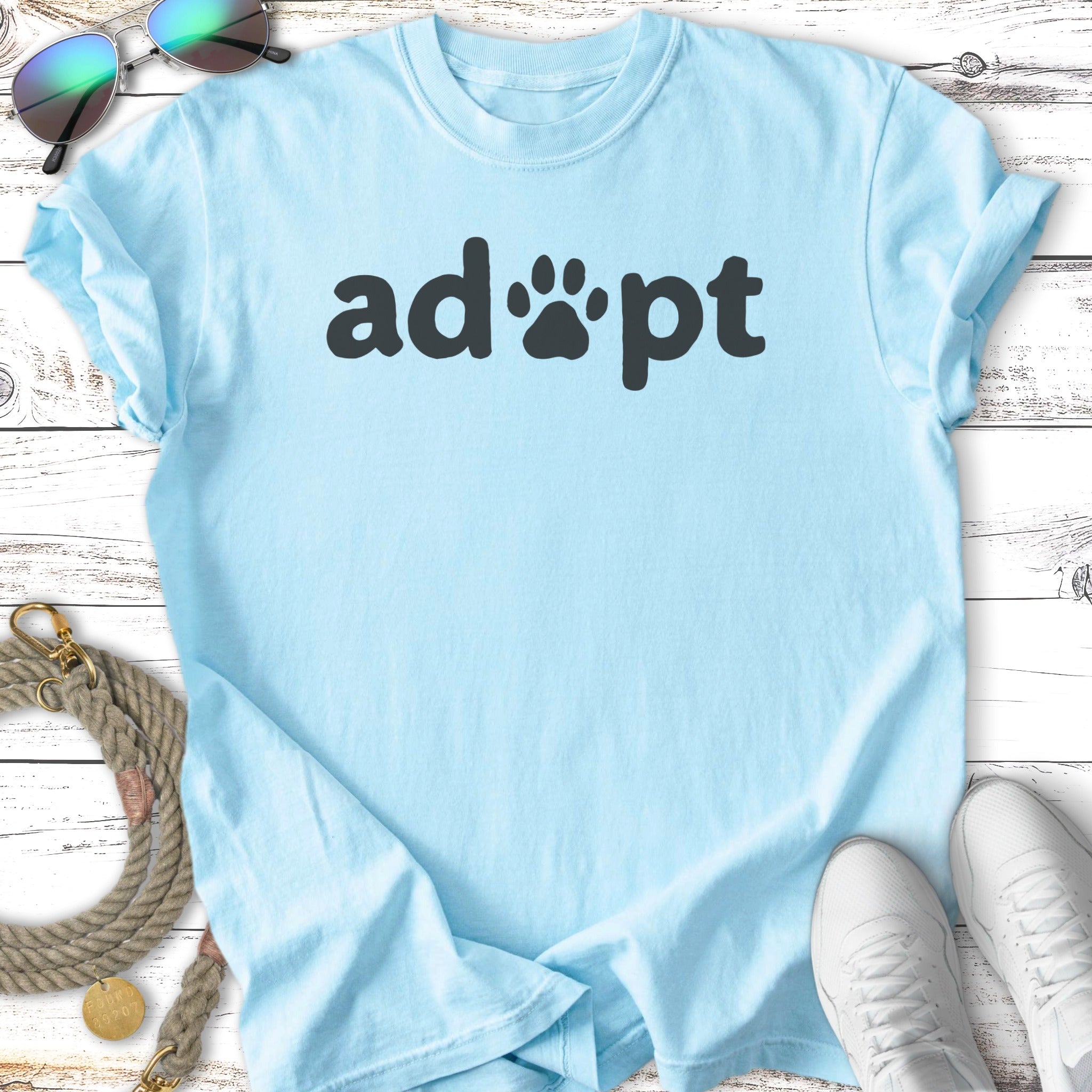 Light blue t-shirt with "adopt" in black lettering, next to pet accessories.