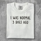 White t-shirt with "I WAS NORMAL 3 DOGS AGO" printed in black text.