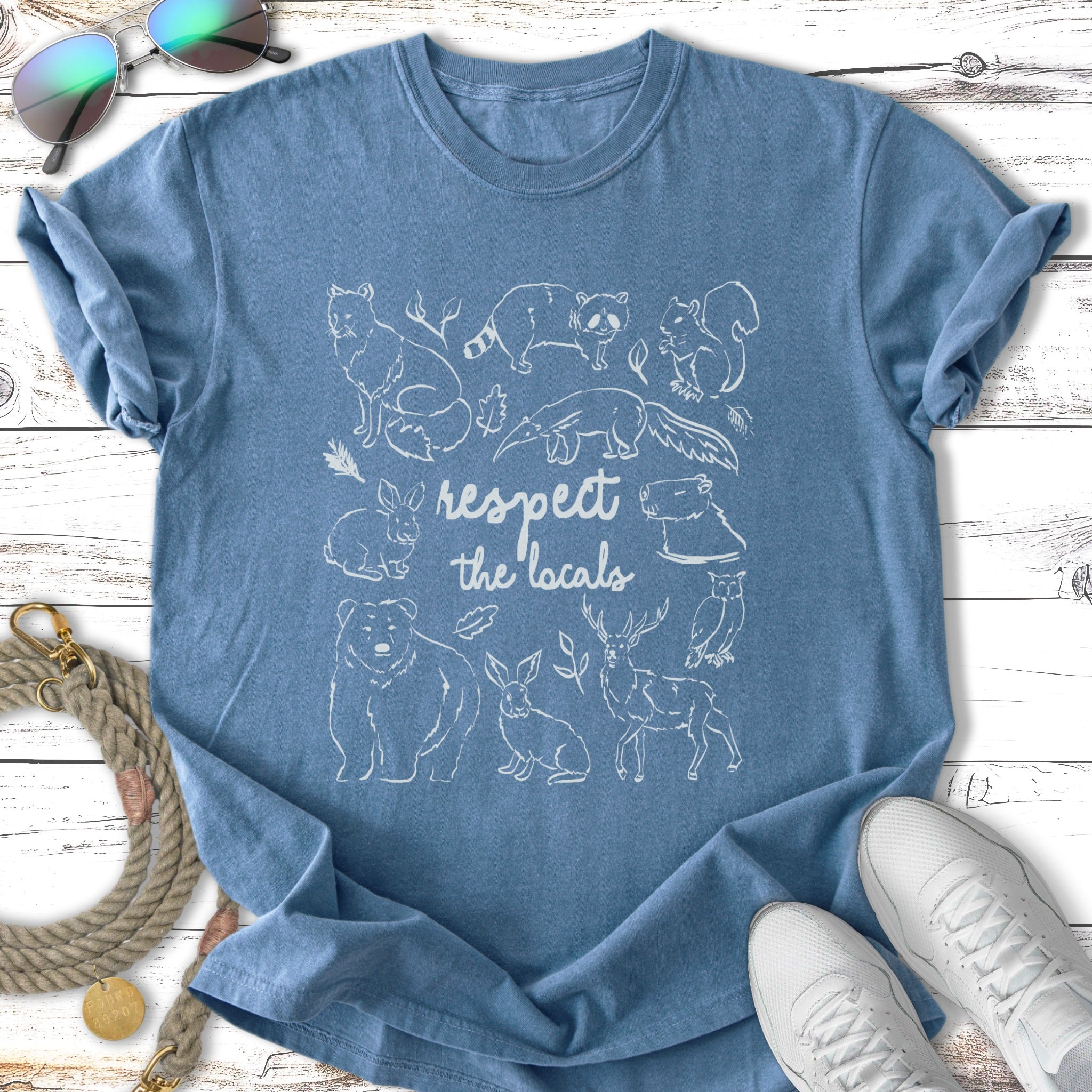 Blue t-shirt with a white line drawing of woodland animals and text "respect the locals".