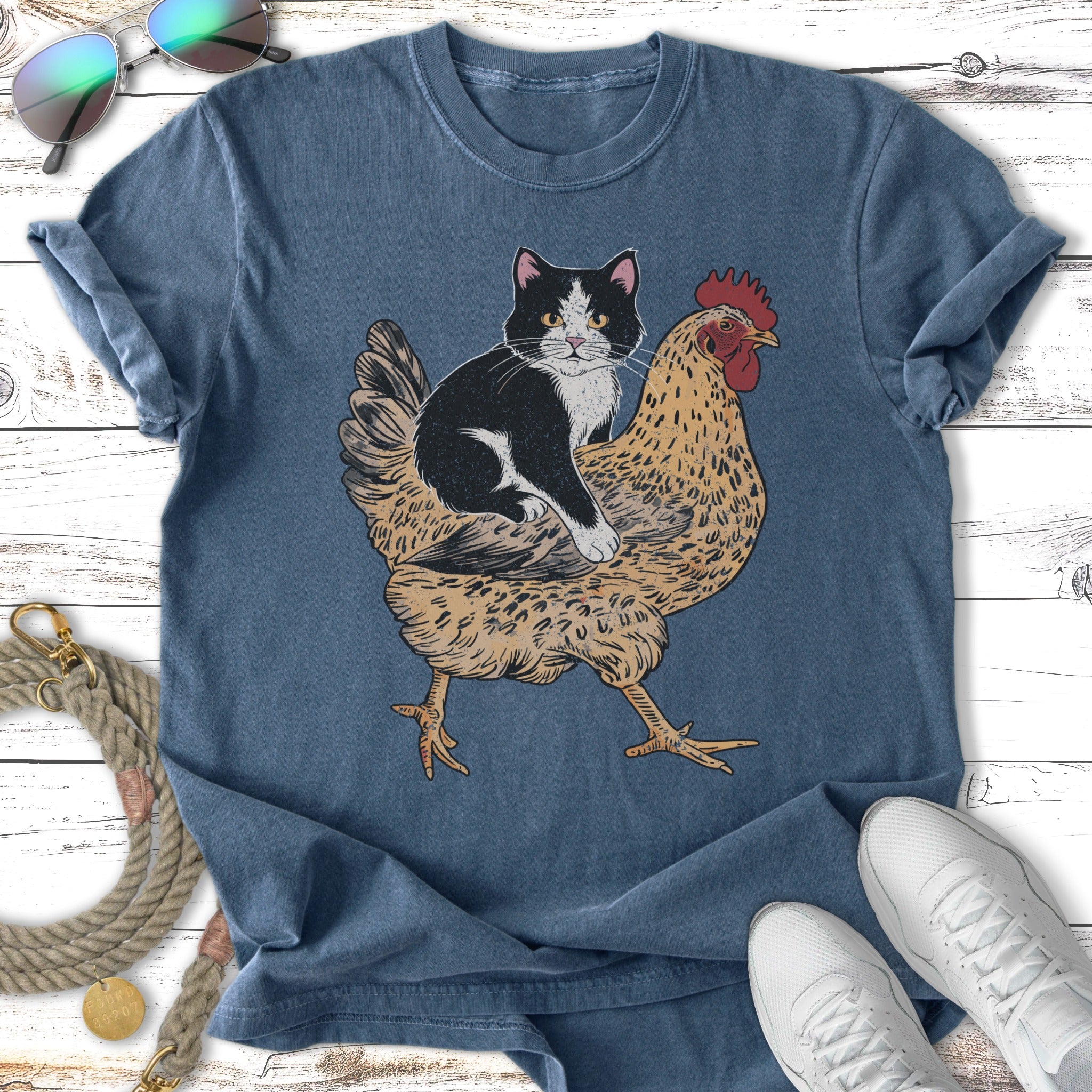 Black and white cat sits on a chicken illustration on a dark blue t-shirt.