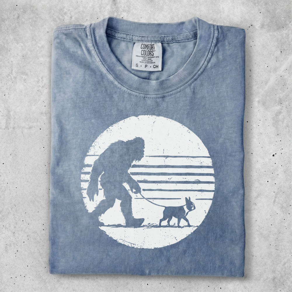 T-shirt with Bigfoot walking a dog in a circle motif.