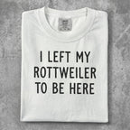 White t-shirt with "I LEFT MY ROTTWEILER TO BE HERE" in black text.