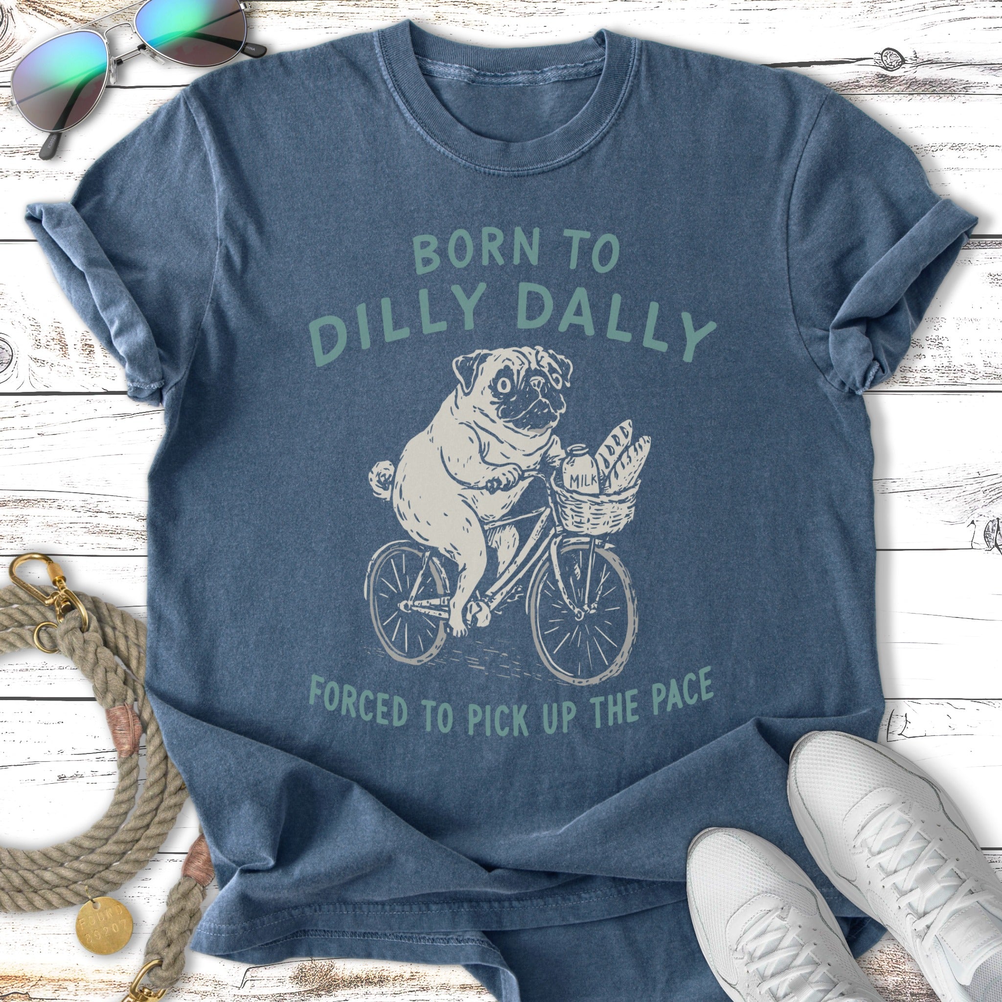 Pug riding bicycle with baguette, "Born to Dilly Dally" shirt.