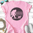 Pink t-shirt featuring a silhouette of Bigfoot walking a small dog on a leash.