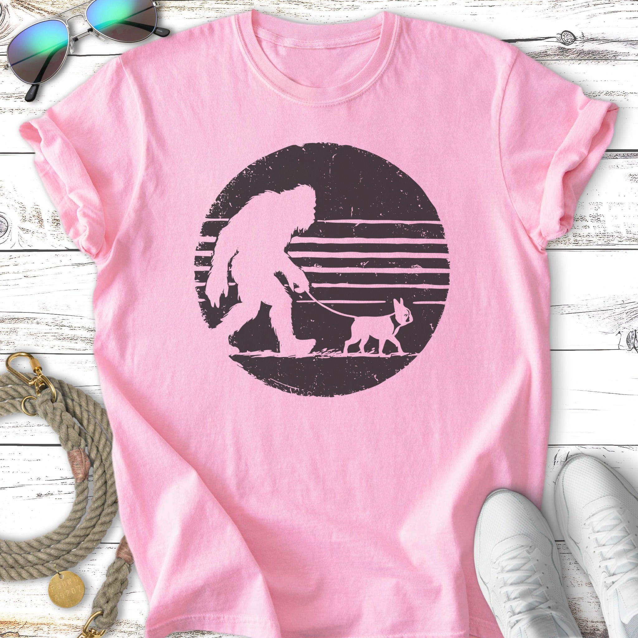 Pink t-shirt featuring a silhouette of Bigfoot walking a small dog on a leash.