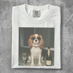 Cavalier King Charles Spaniel wearing sunglasses next to champagne bottle and flute.