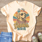 Peach t-shirt with distressed graphic of a golden retriever wearing sunglasses and bandana, text "In My Golden Era".