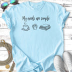 Light blue t-shirt with "My needs are simple" text and icons of coffee, paw print, and books.