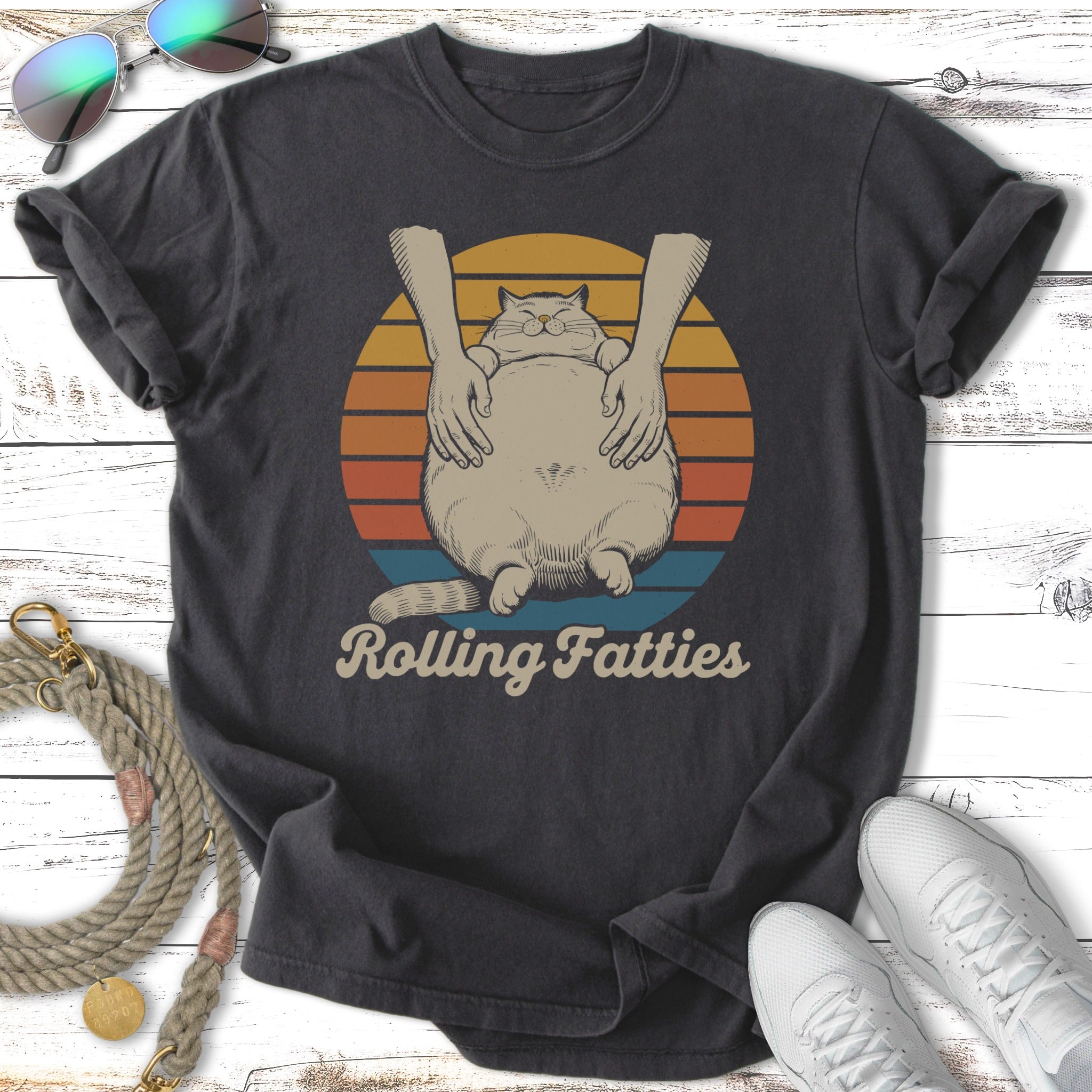 T-shirt graphic with fat cat being held by hands, sunset background, "Rolling Fatties" text.