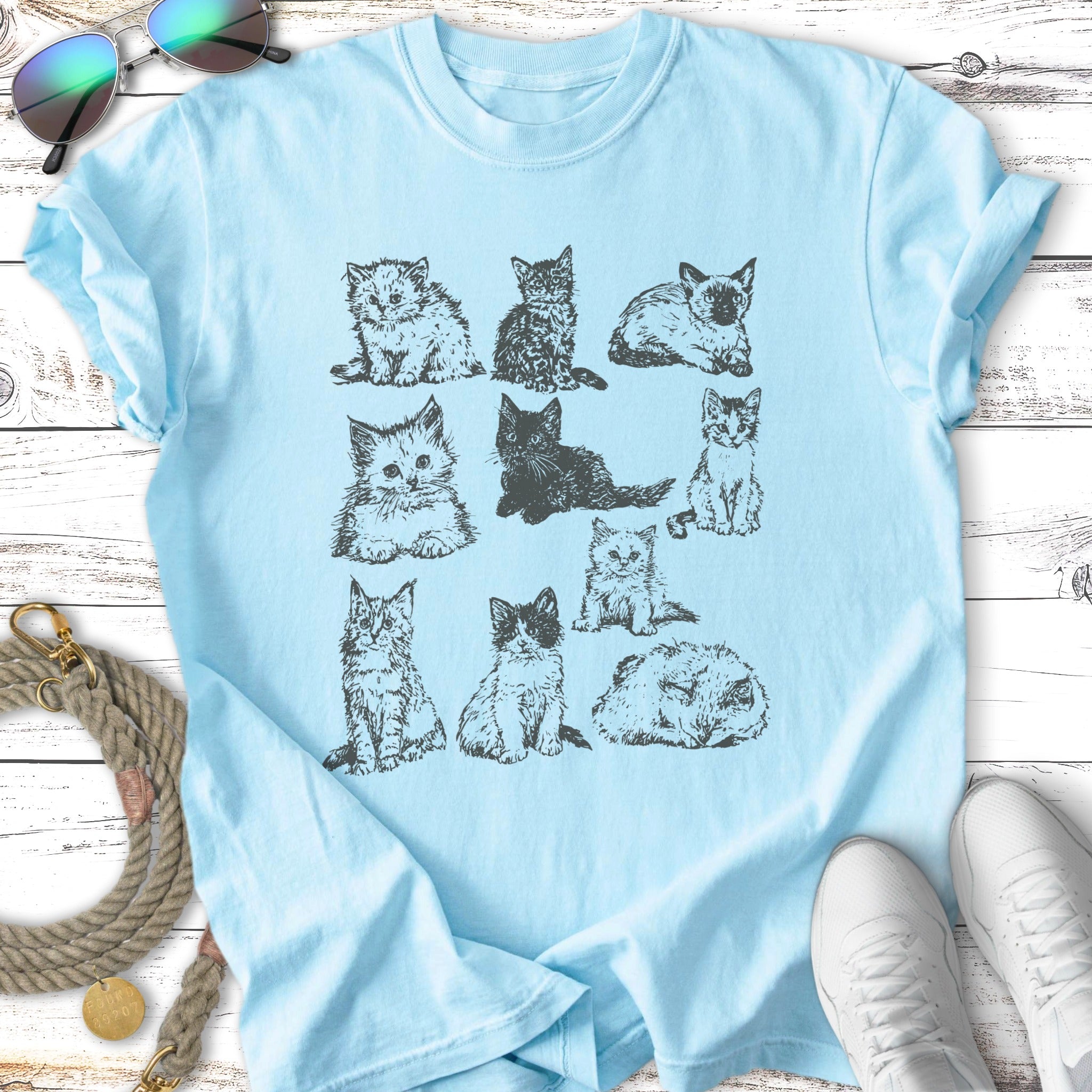 Nine different kitten illustrations on a light blue t-shirt.