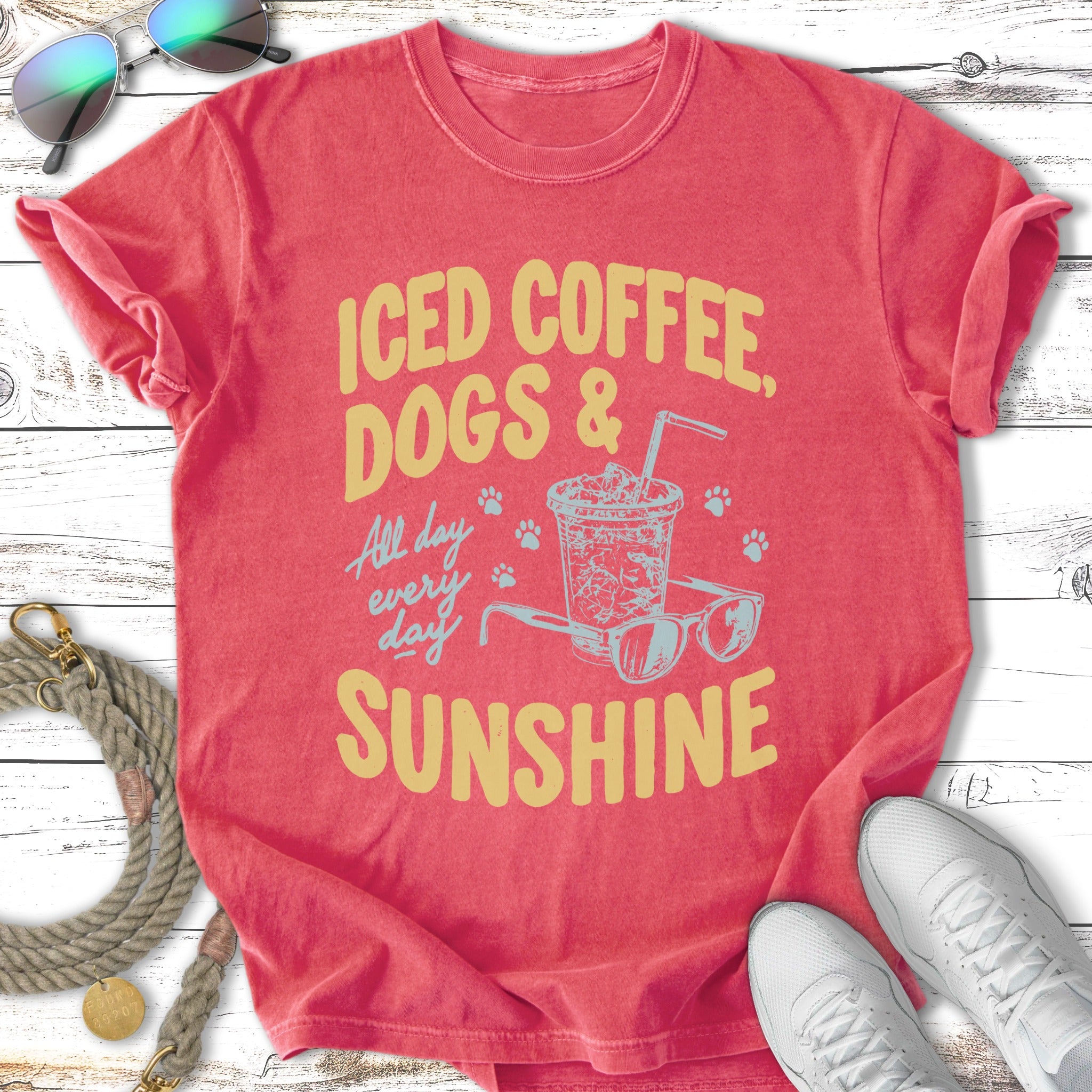 Iced coffee, dogs, and sunshine graphic on a coral t-shirt with sunglasses and sneakers.