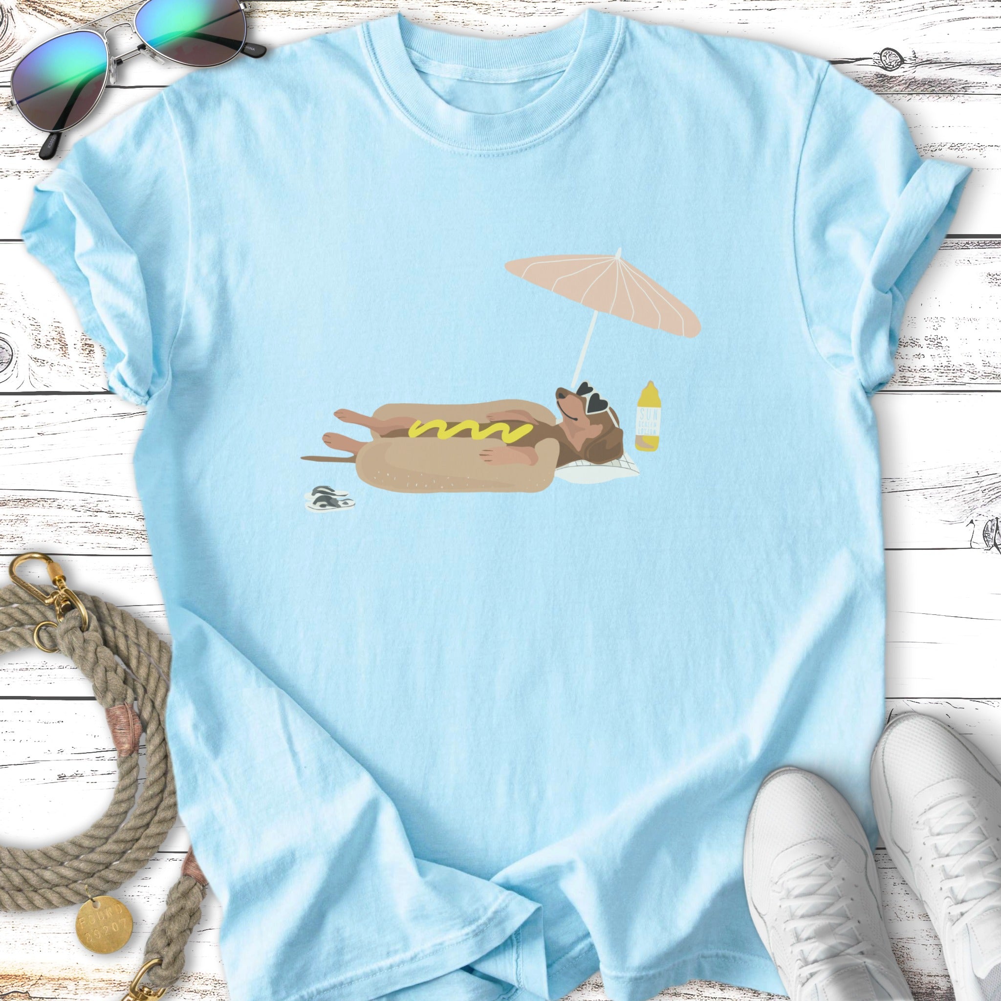 Light blue t-shirt with a cartoon dachshund on a hot dog float under an umbrella.