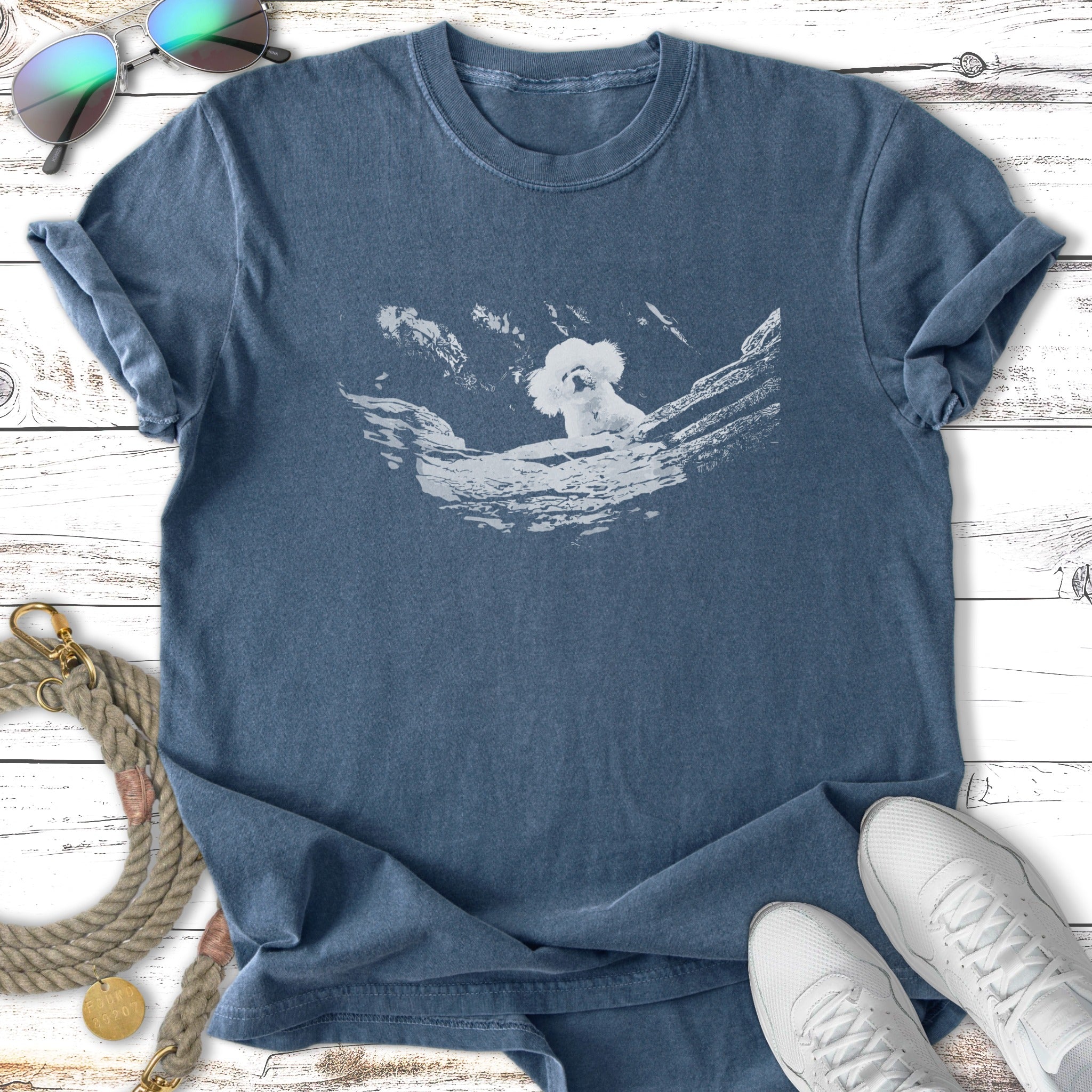 Blue t-shirt with white graphic of a fluffy dog in a rocky landscape.