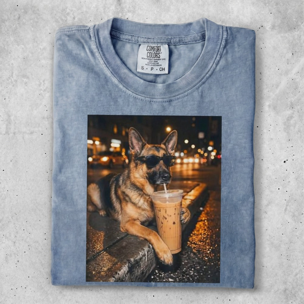 German Shepherd wearing sunglasses sips iced coffee on a city street.