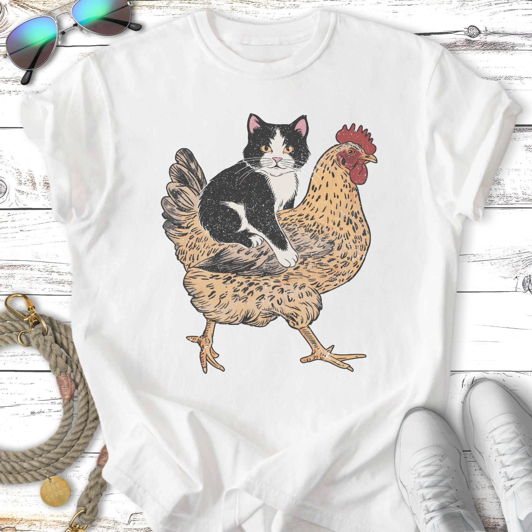Black and white cat riding a chicken, graphic print on white t-shirt.
