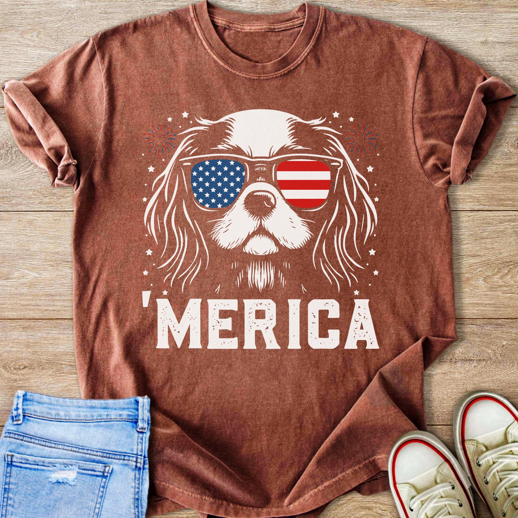 Dog wearing American flag sunglasses and "MERICA" text on a rust-colored t-shirt.