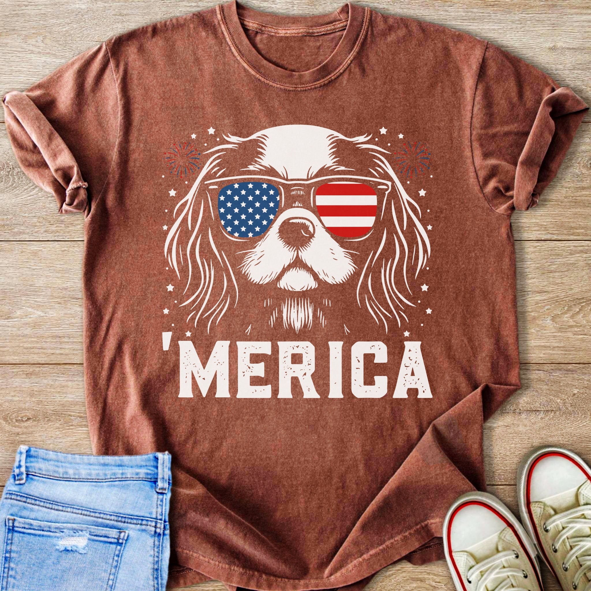 Dog wearing American flag sunglasses and "MERICA" text on a rust-colored t-shirt.