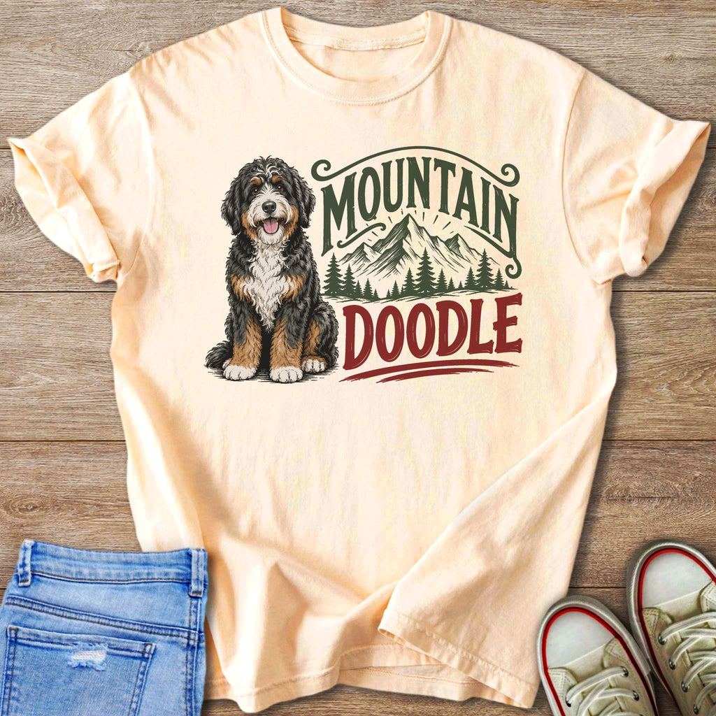 Peach t-shirt with a doodle dog sitting, mountains, and text.