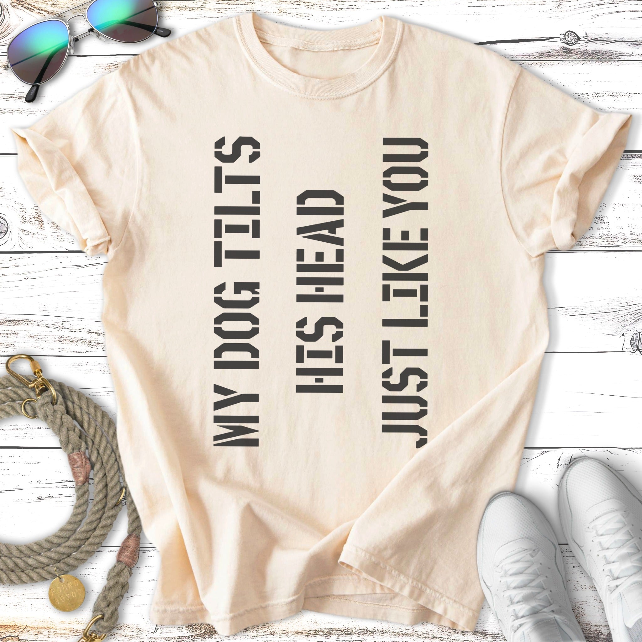 Light beige t-shirt with text "MY DOG TILTS HIS HEAD JUST LIKE YOU" in black.