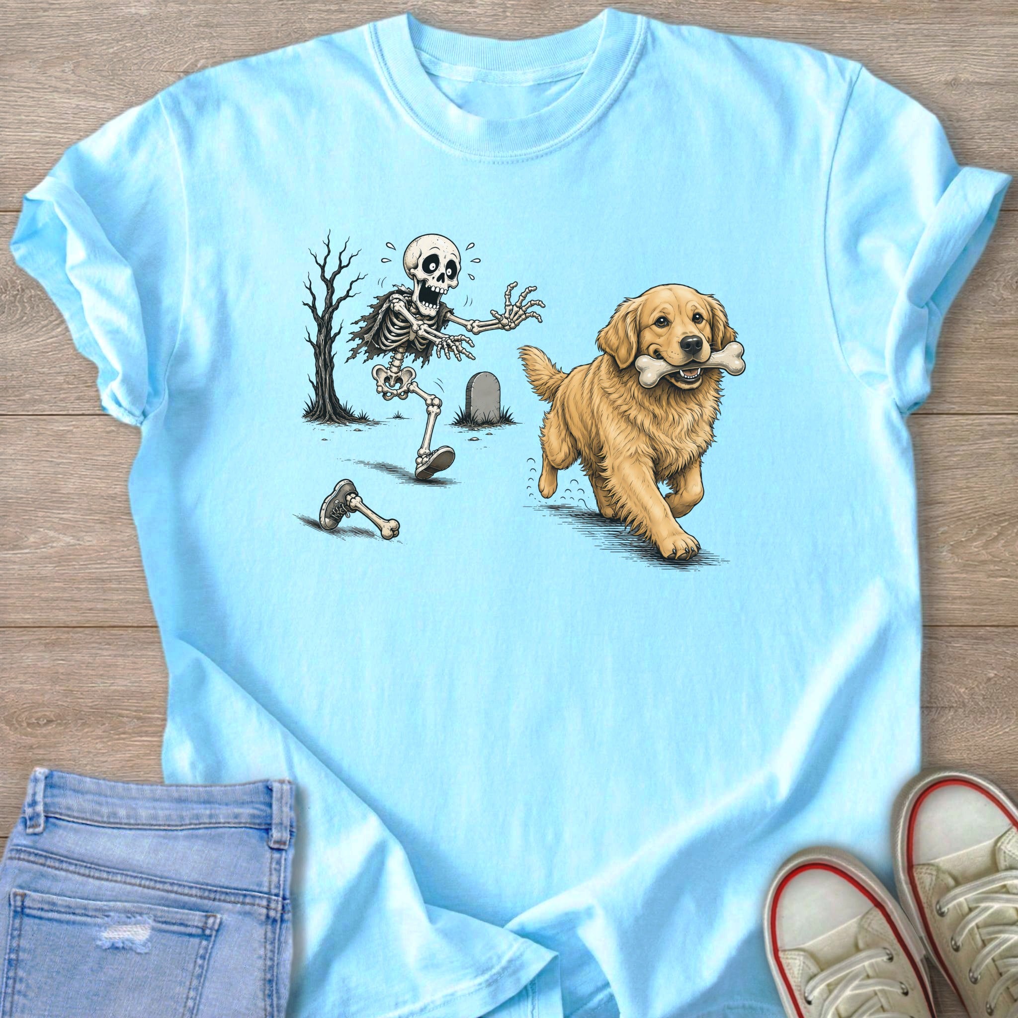 Skeleton running from a golden retriever holding a bone on a light blue t-shirt.